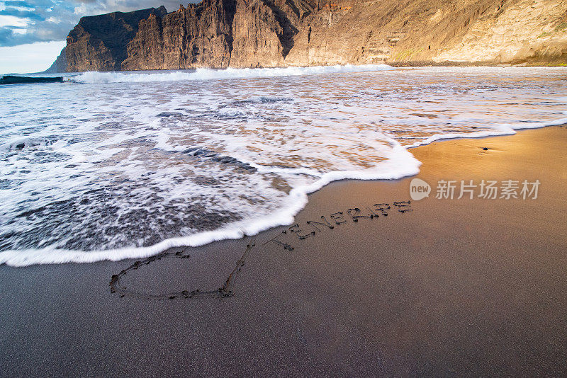 单字特内里费写在沙旁边画的心形状在Playa de Los Gigantes，特内里费，加那利群岛，西班牙-股票照片